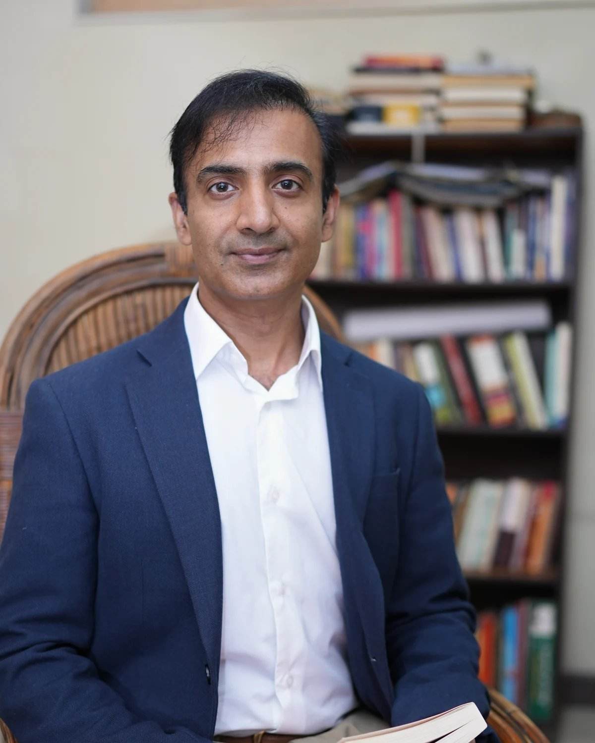Rai Shahnawaz seated in front of his bookshelf, holding a book